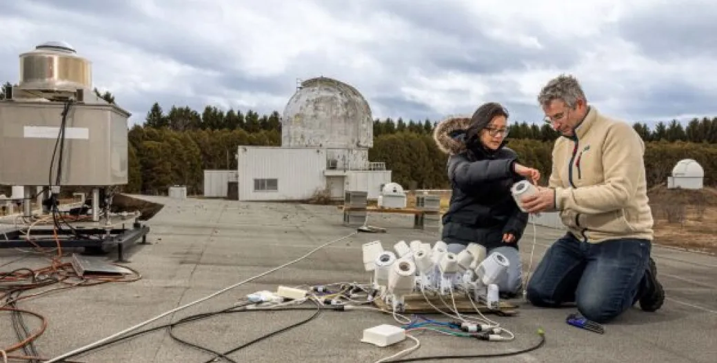 Tammy Do and Michael Mazur kneel beside meteor-monitoring cameras on the roof of Elginfield Observatory in Ontario.